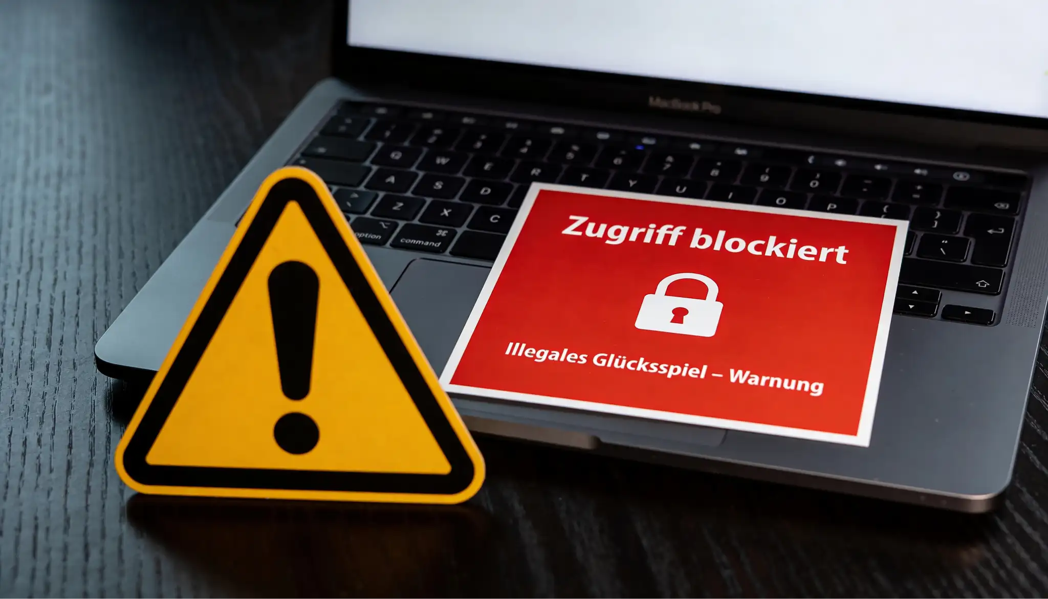 Warnschild vor einem Laptop mit gesperrter Wettseite als Symbol fuer den Schwarzmarkt bei Pferdewetten